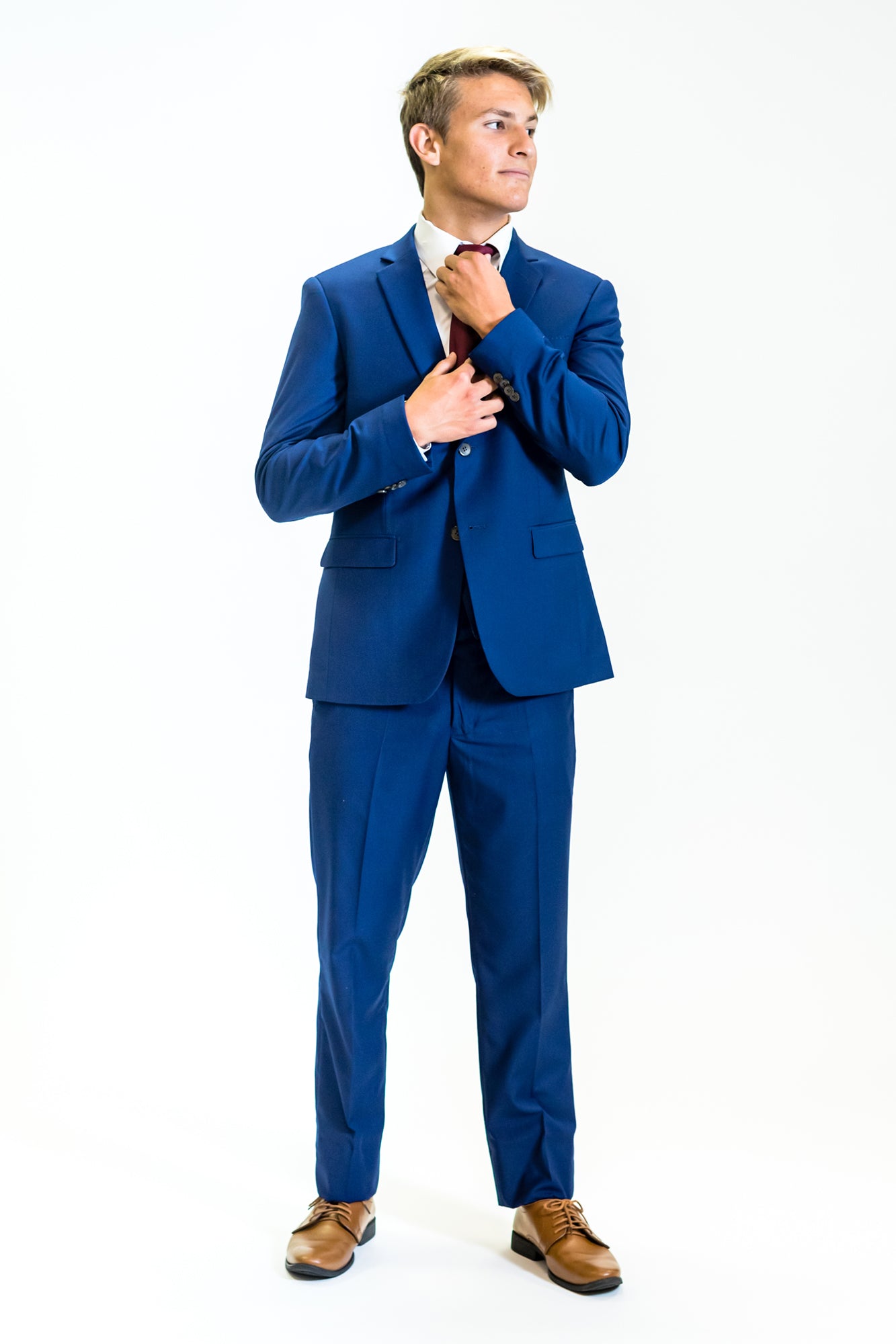 high school student boy wearing cobalt blue suit standing frontward adjusting red tie